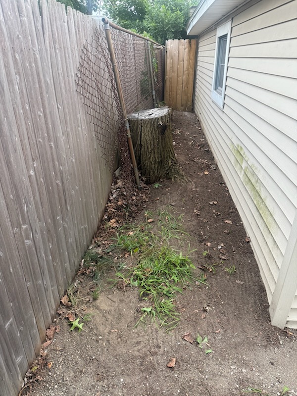 Narrow walkway along chainlink and wood fence cleared around tree stump in Holyoke MA