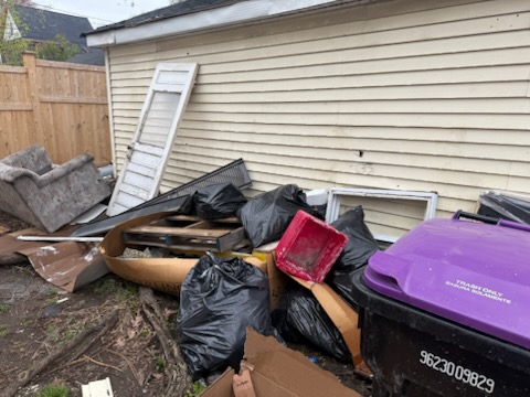 Bulky upholstered armchair, wooden panel door, wood pallets and bagged junk piled beside garage in Springfield MA