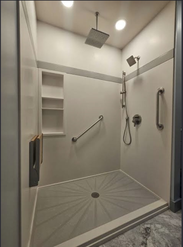 Walk-in shower with overhead rain head, grab bars, and recessed shelves