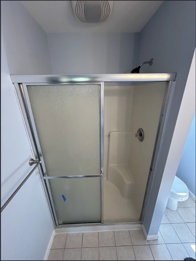 Walk-in shower enclosure with sliding glass door and built-in corner bench