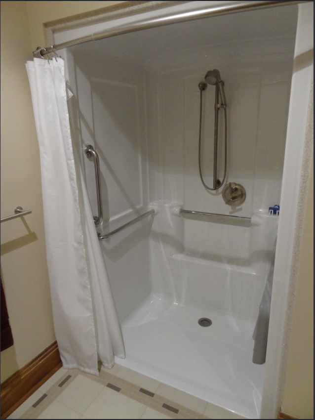 Walk-in shower enclosure with molded seat, handheld shower, and safety grab bars