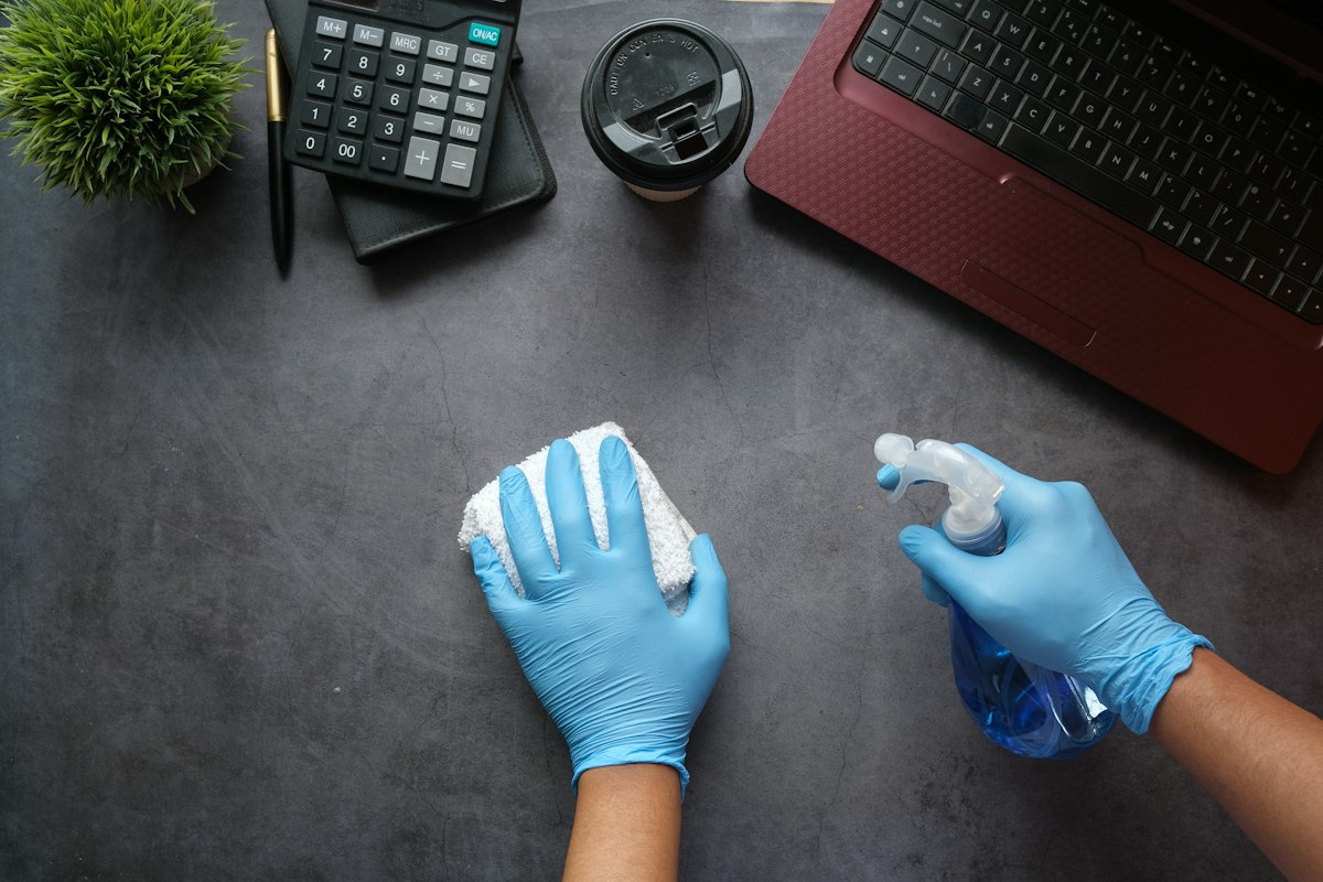Cleaner in gloves disinfecting an office desk