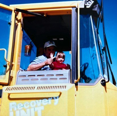 Jade as a toddler in the cab of a yellow recovery truck