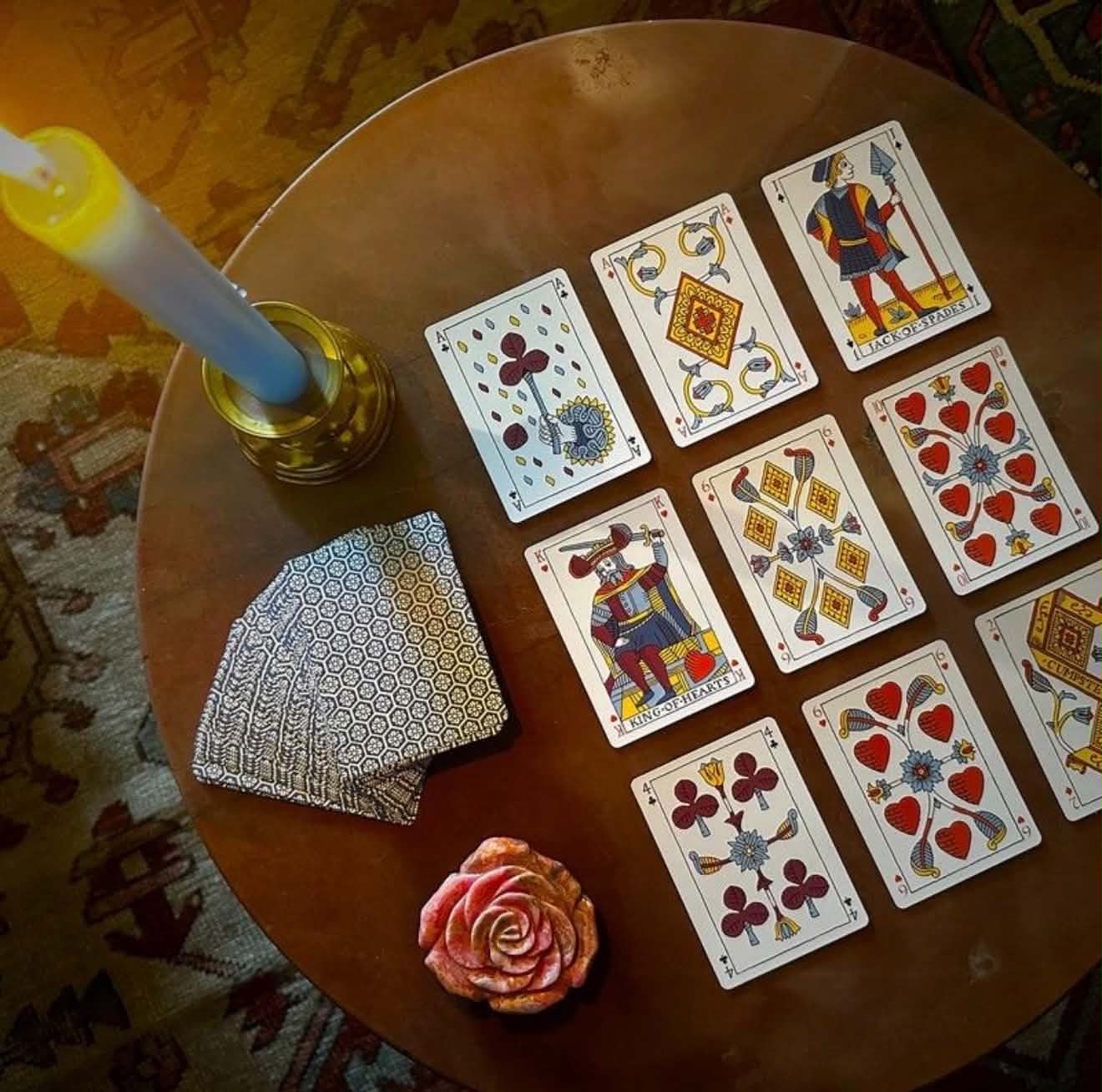 Cartomancy reading table with antique playing cards, candle, and carved rose