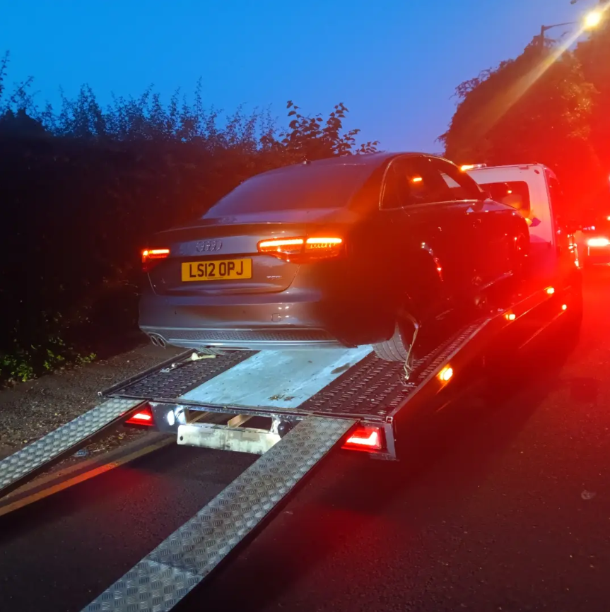 Audi saloon recovered onto flatbed recovery truck with amber beacons active at night