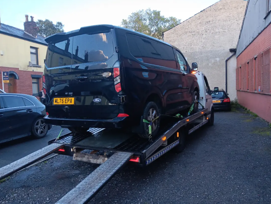 Black Ford van safely secured and loaded onto recovery flatbed truck
