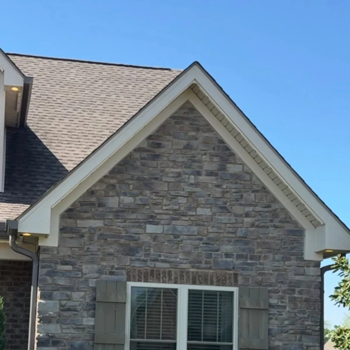 Daytime view of discreet roofline track installed flush under soffit along a stone and brick home.
