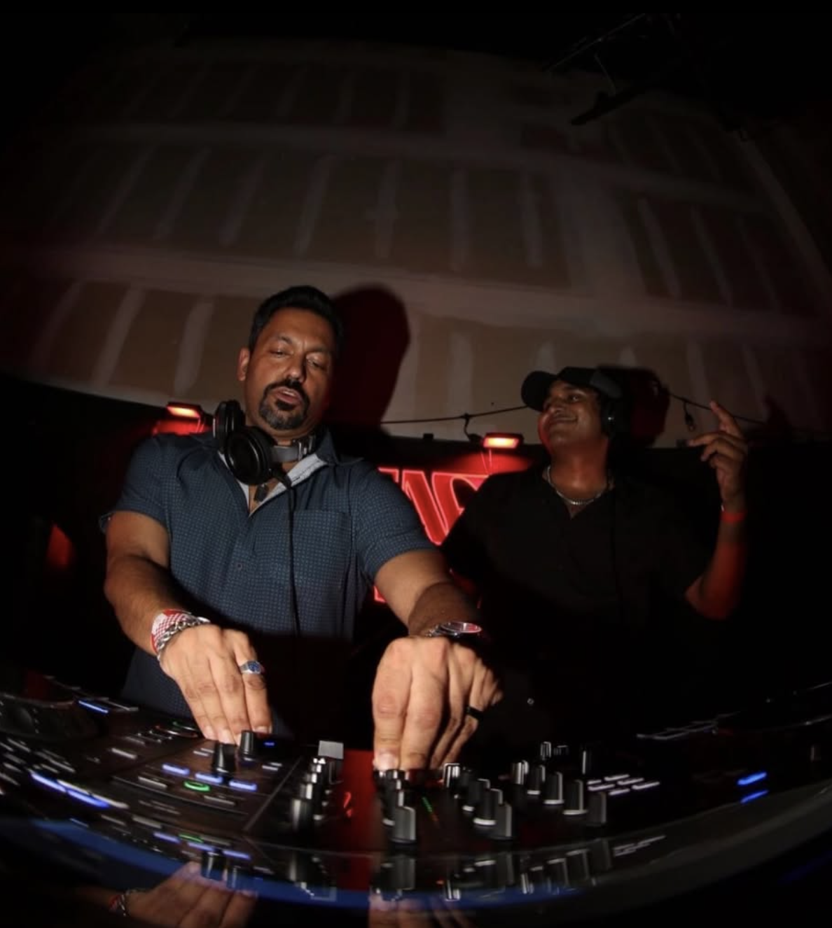 Curry Fury close-up mixing on the Pioneer DJ setup under red club neon lights