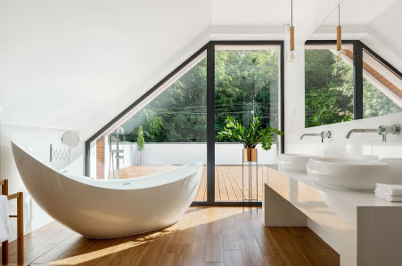 Bright attic ensuite with curved freestanding bath and outdoor balcony view