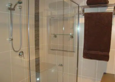 Walk-in glass shower enclosure with chrome tapware and feature strip tiling
