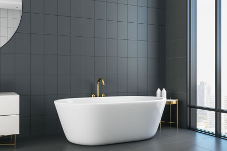 Freestanding bathtub with brushed gold tapware and dark charcoal tiles
