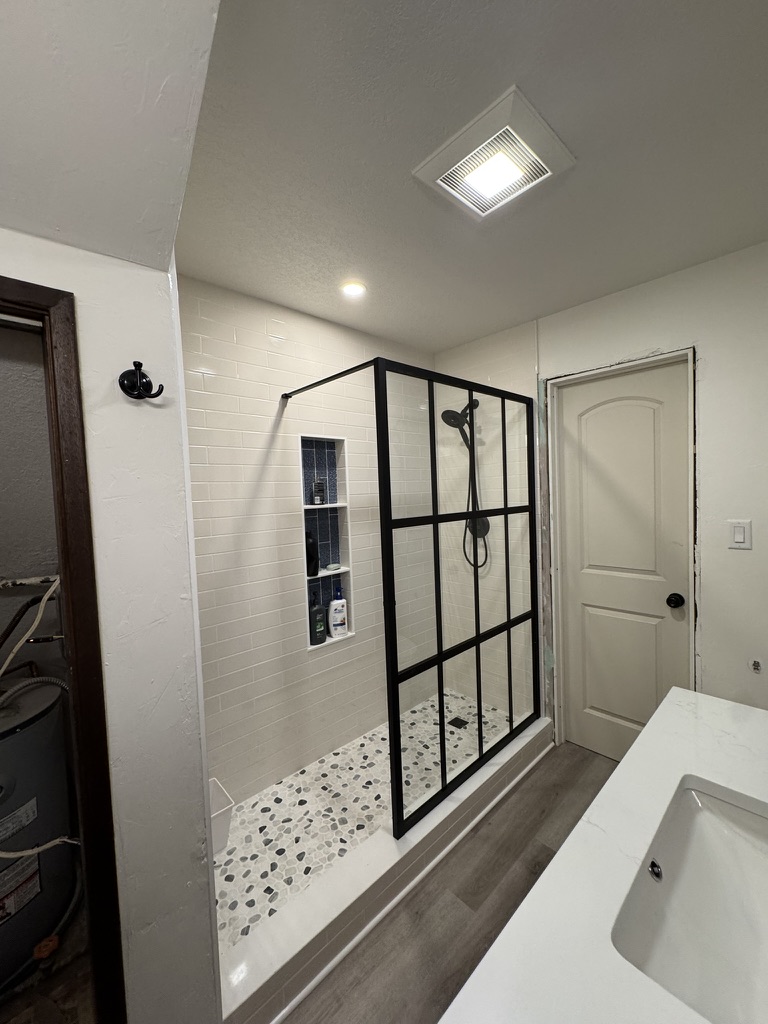 Completed custom walk-in tile shower with glass grid door and pebble floor