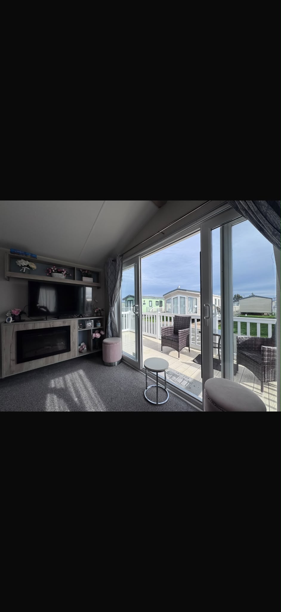 Bright lounge area with television, electric fireplace and patio doors opening onto decking