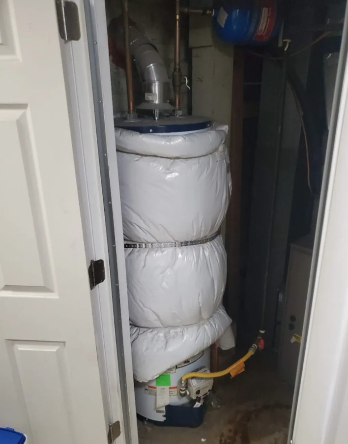 Older water heater wrapped in an insulation blanket in a utility closet