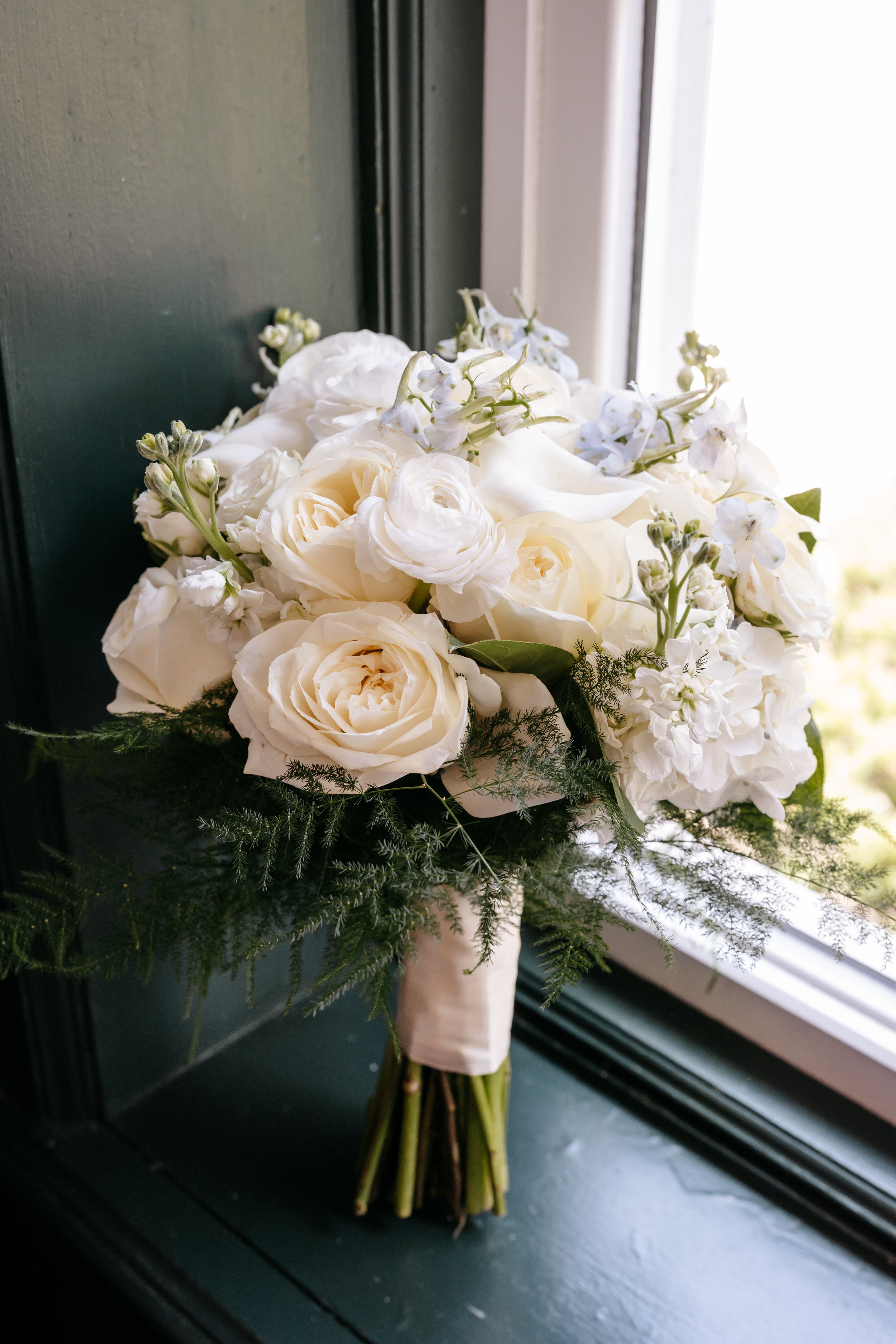 Elegant white bridal bouquet with roses and calla lilies resting on a window sill