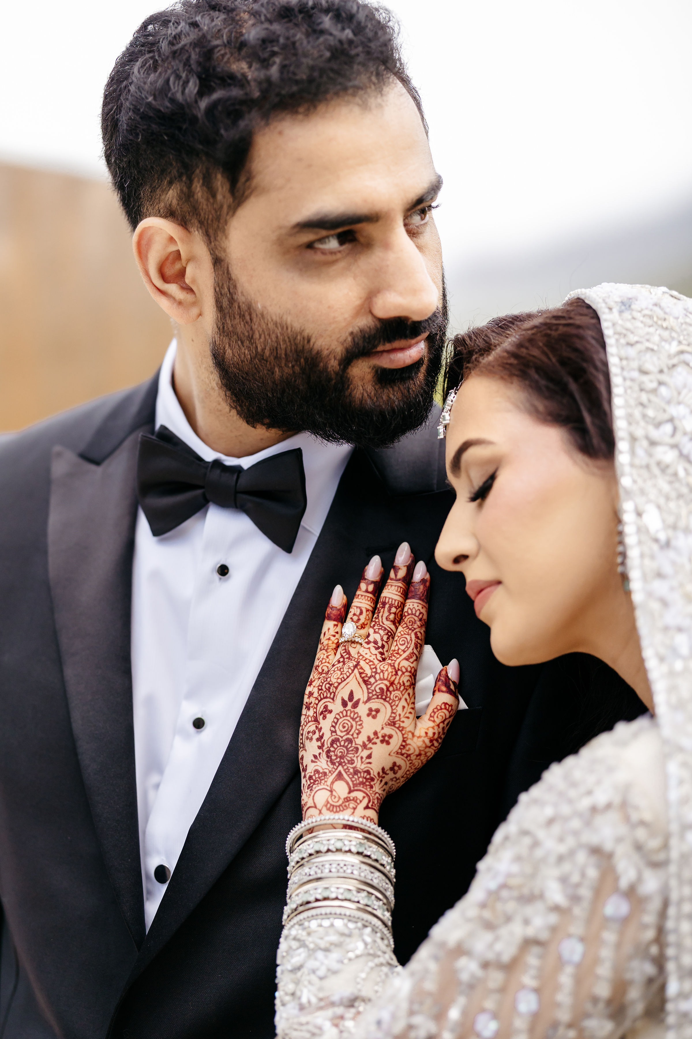 Intimate portrait of bride with intricate henna mehndi resting gently against groom in tuxedo