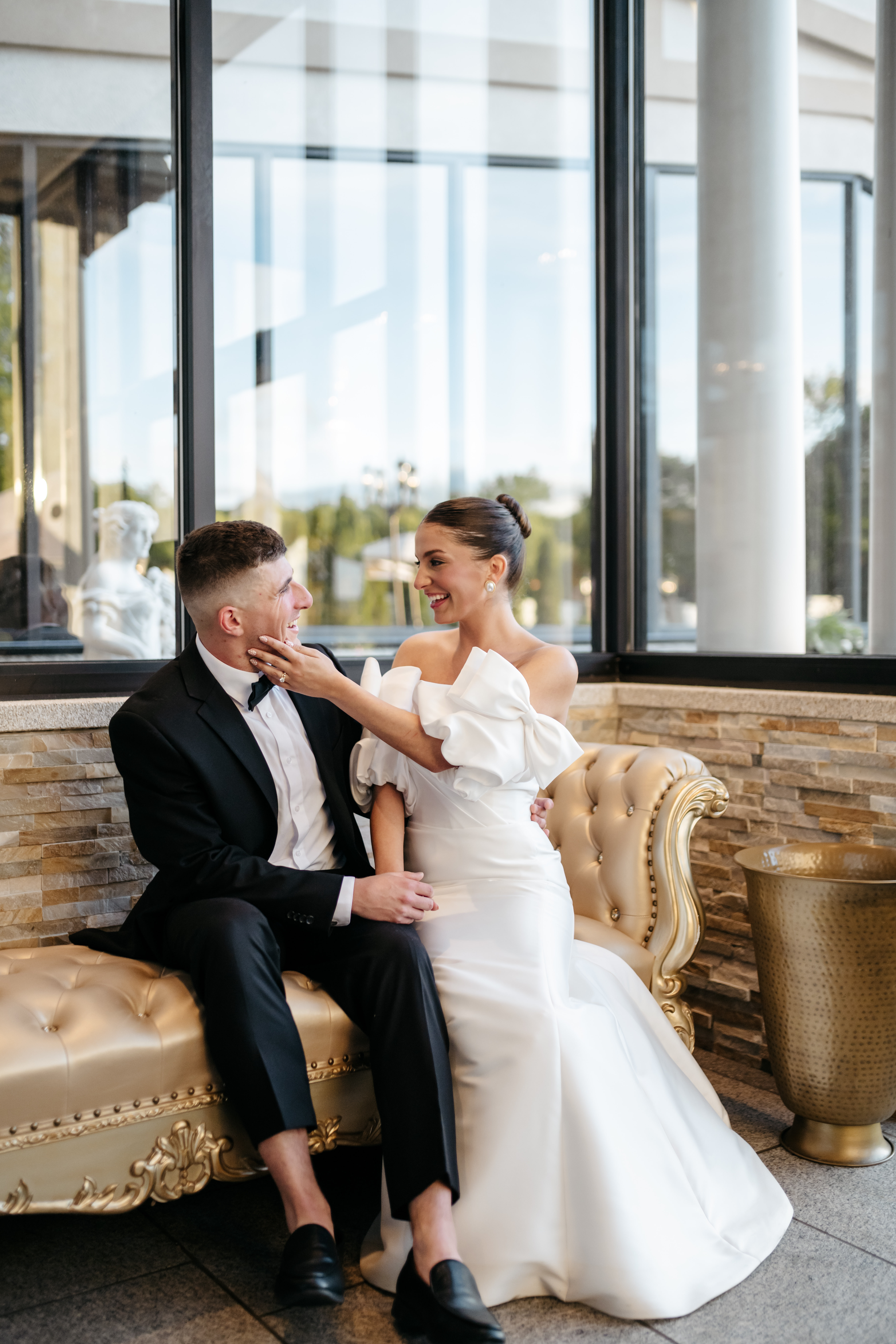 Bride and groom sitting and laughing together on gold settee