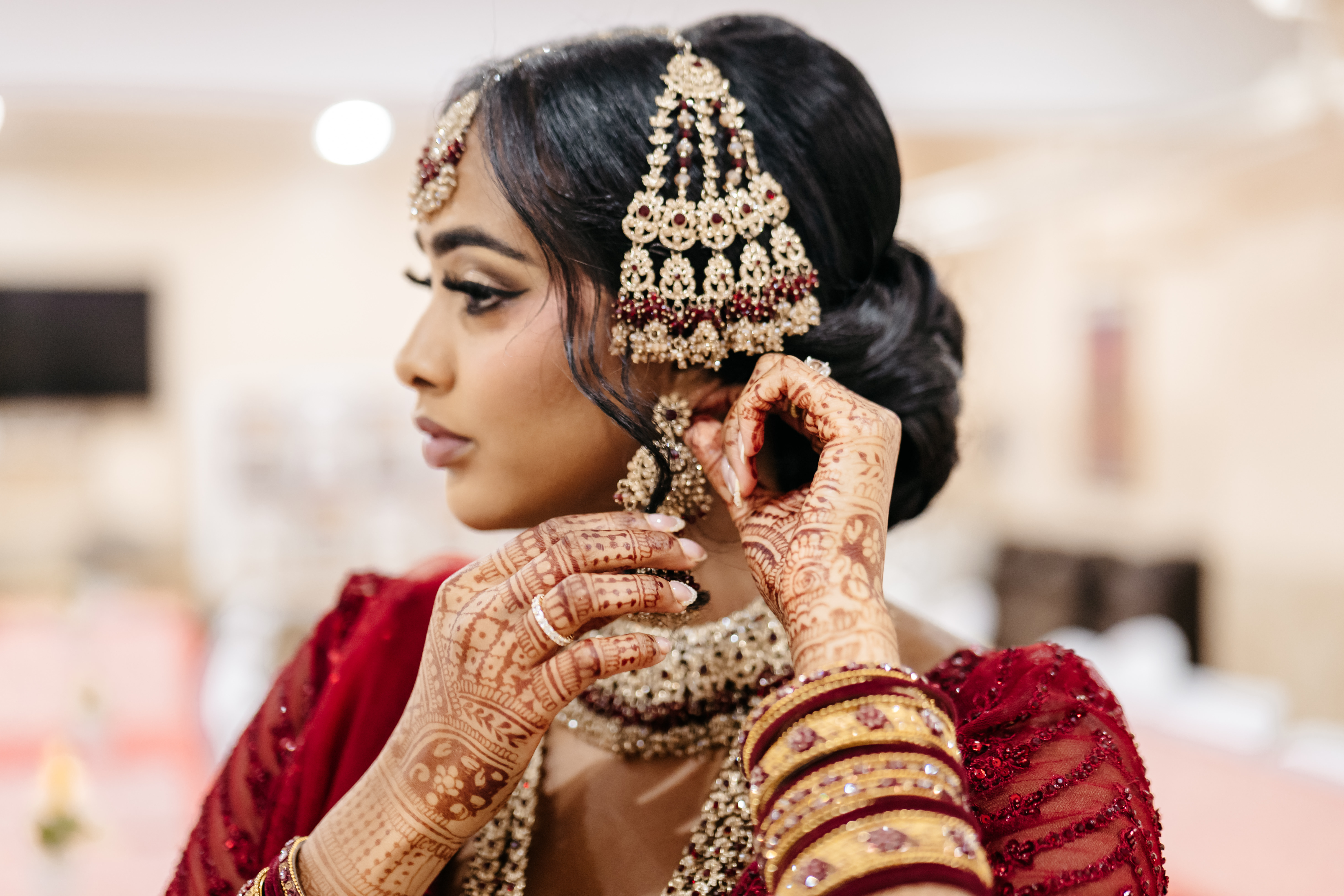 Bride in traditional red wedding attire with intricate mehndi adjusting her gold earring