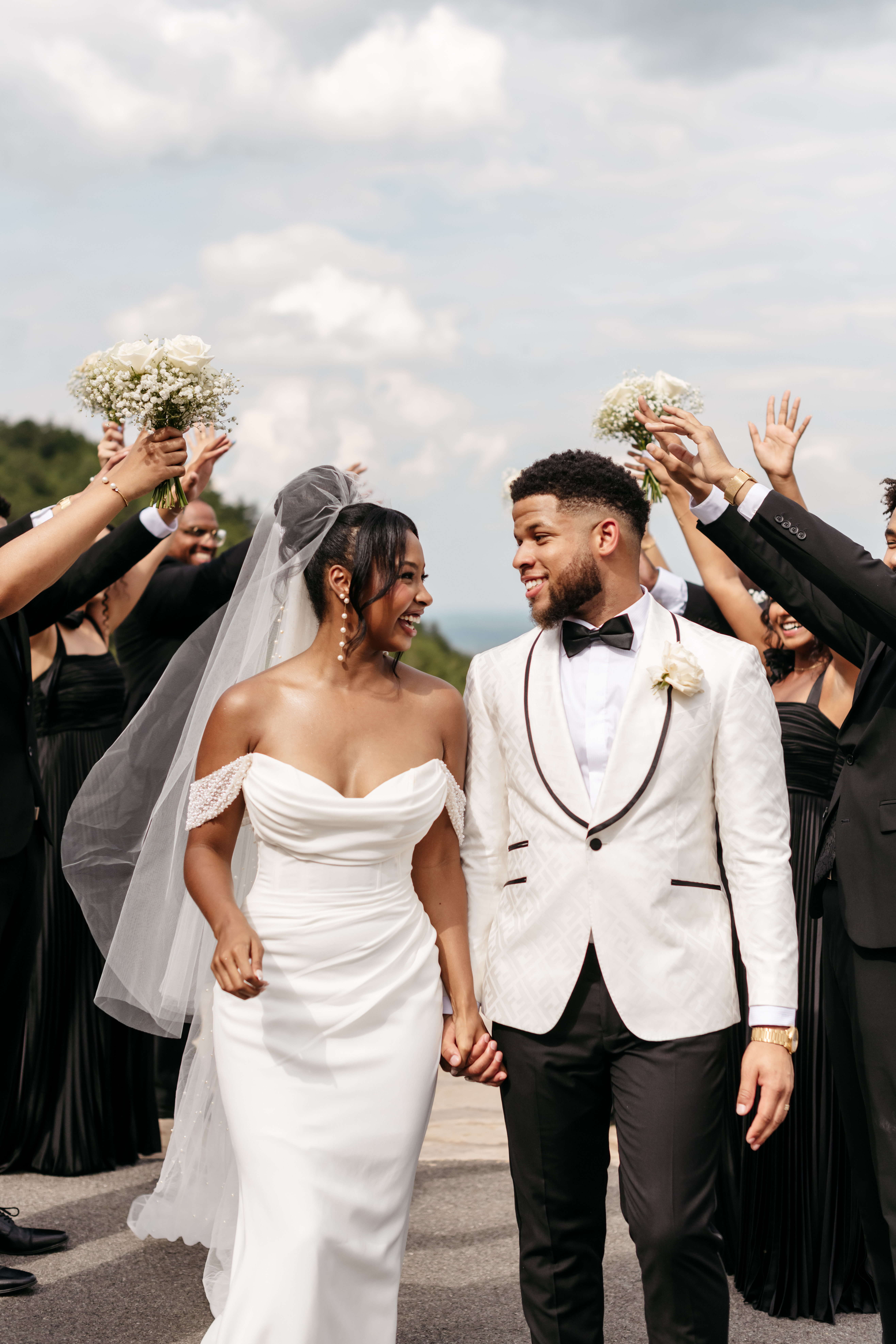 Smiling bride and groom in white tuxedo walking through wedding party tunnel