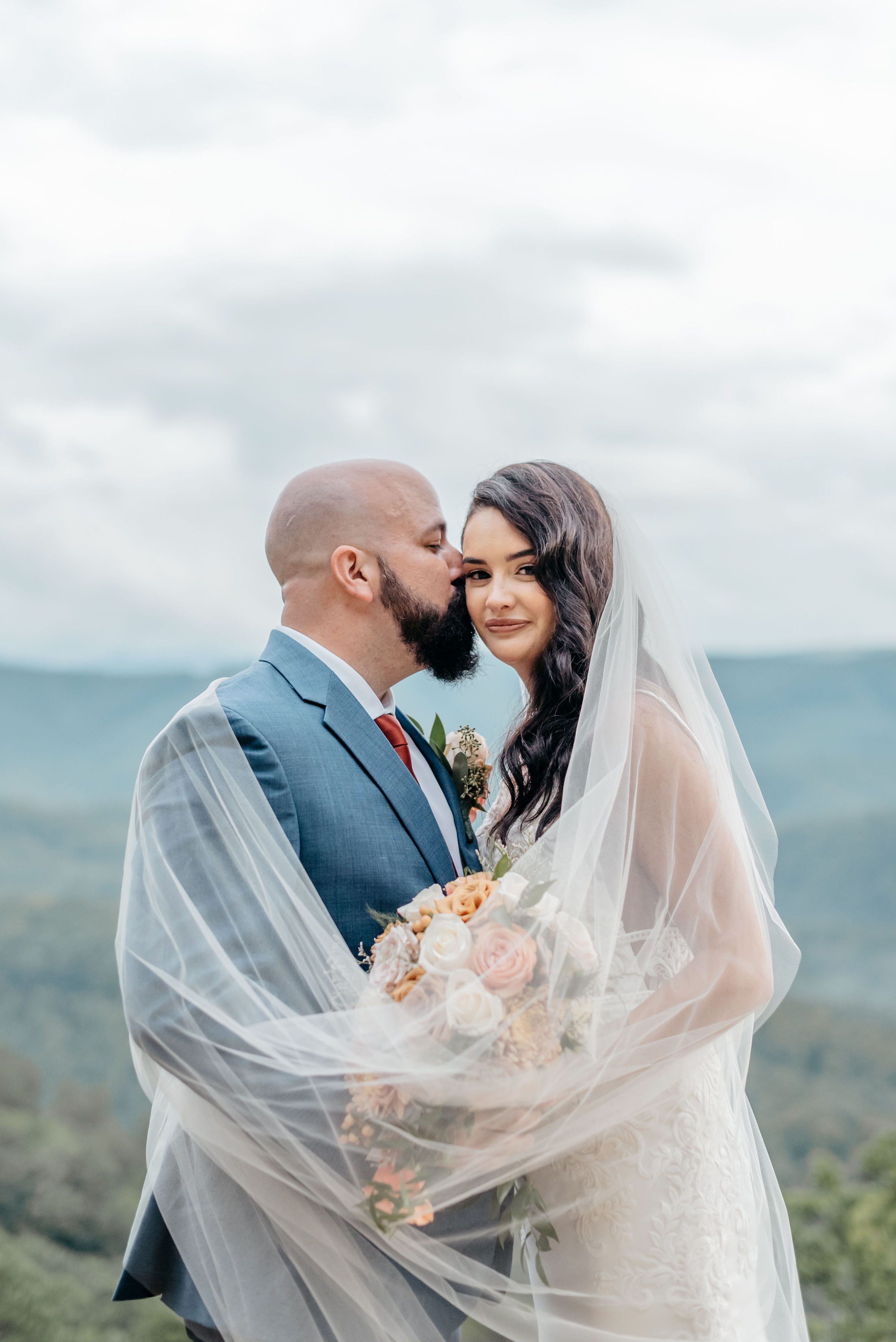 Groom kissing bride under veil with mountain overlook