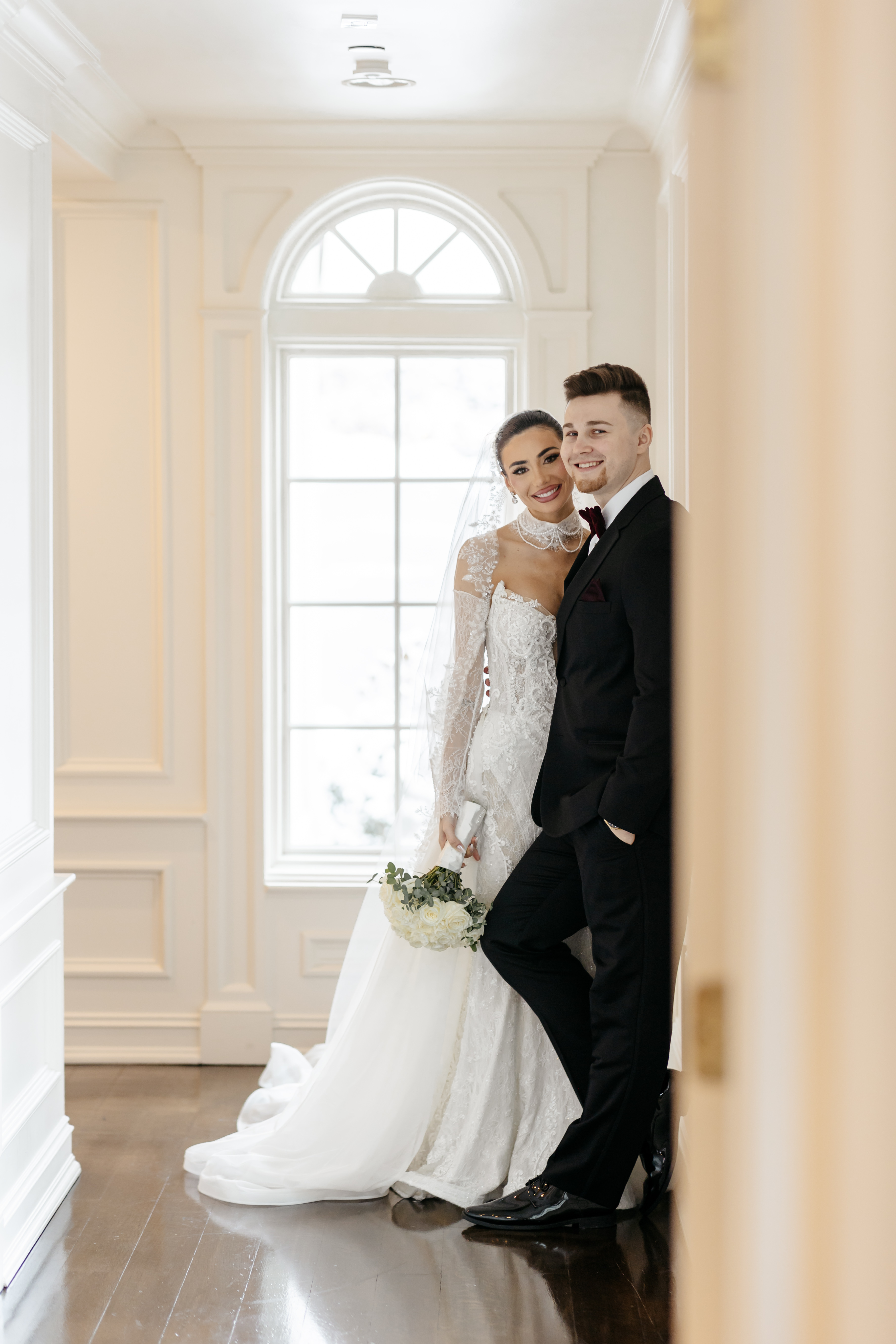 Bride and groom smiling in bright white hallway
