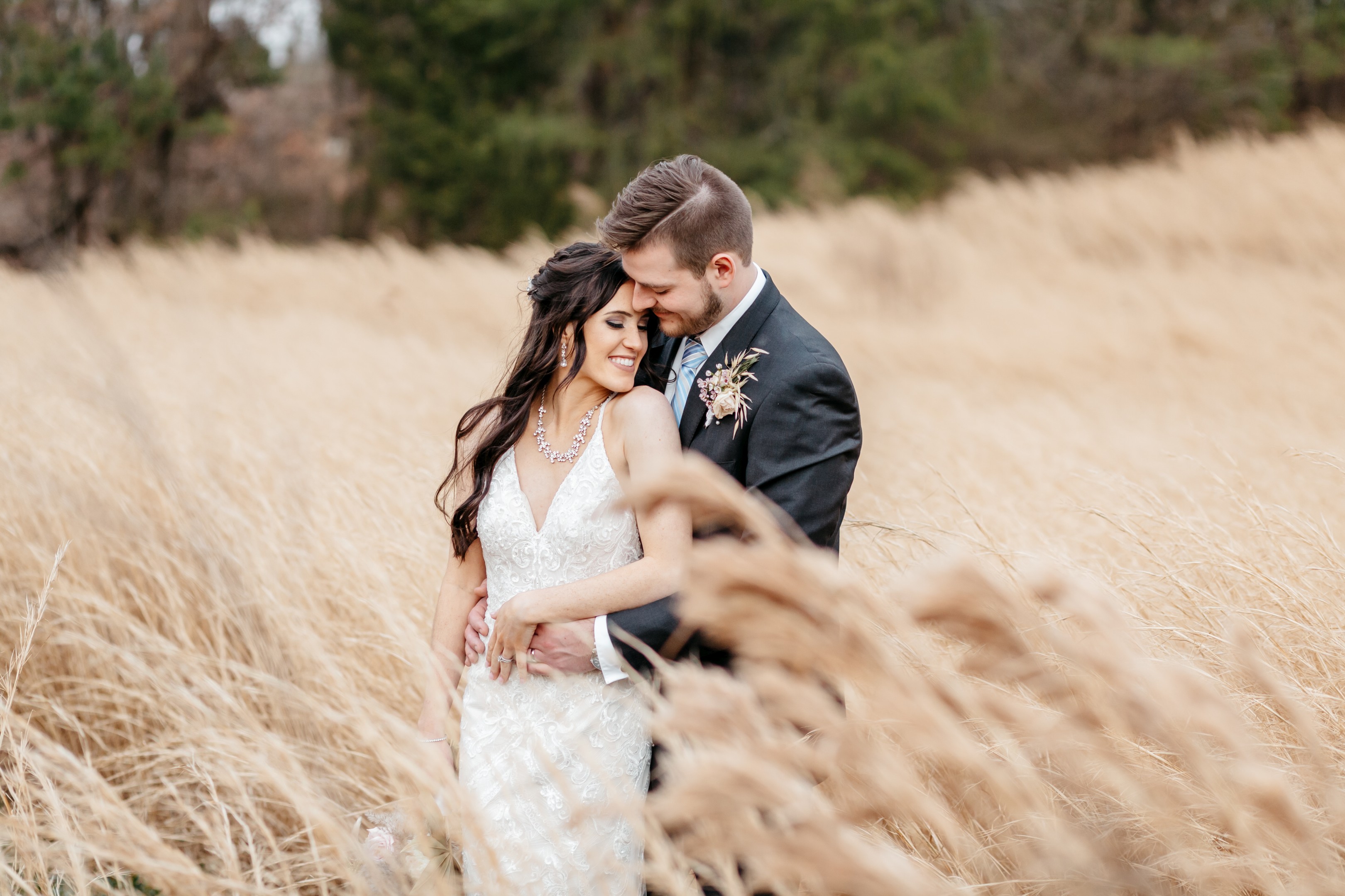 Romantic portrait of bride and groom embracing in a sunlit golden grass field