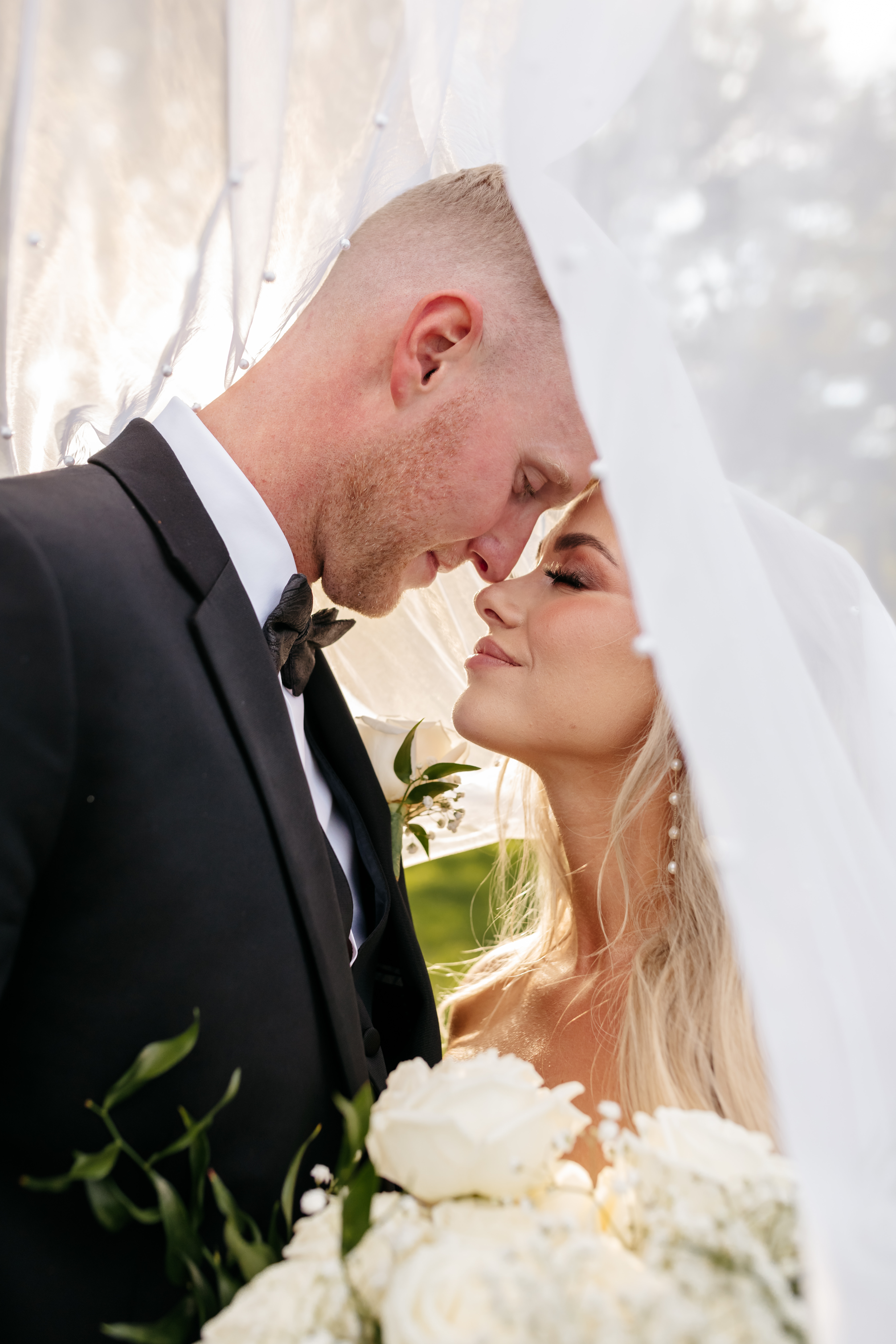 Intimate close-up of bride and groom touching foreheads under pearl bridal veil