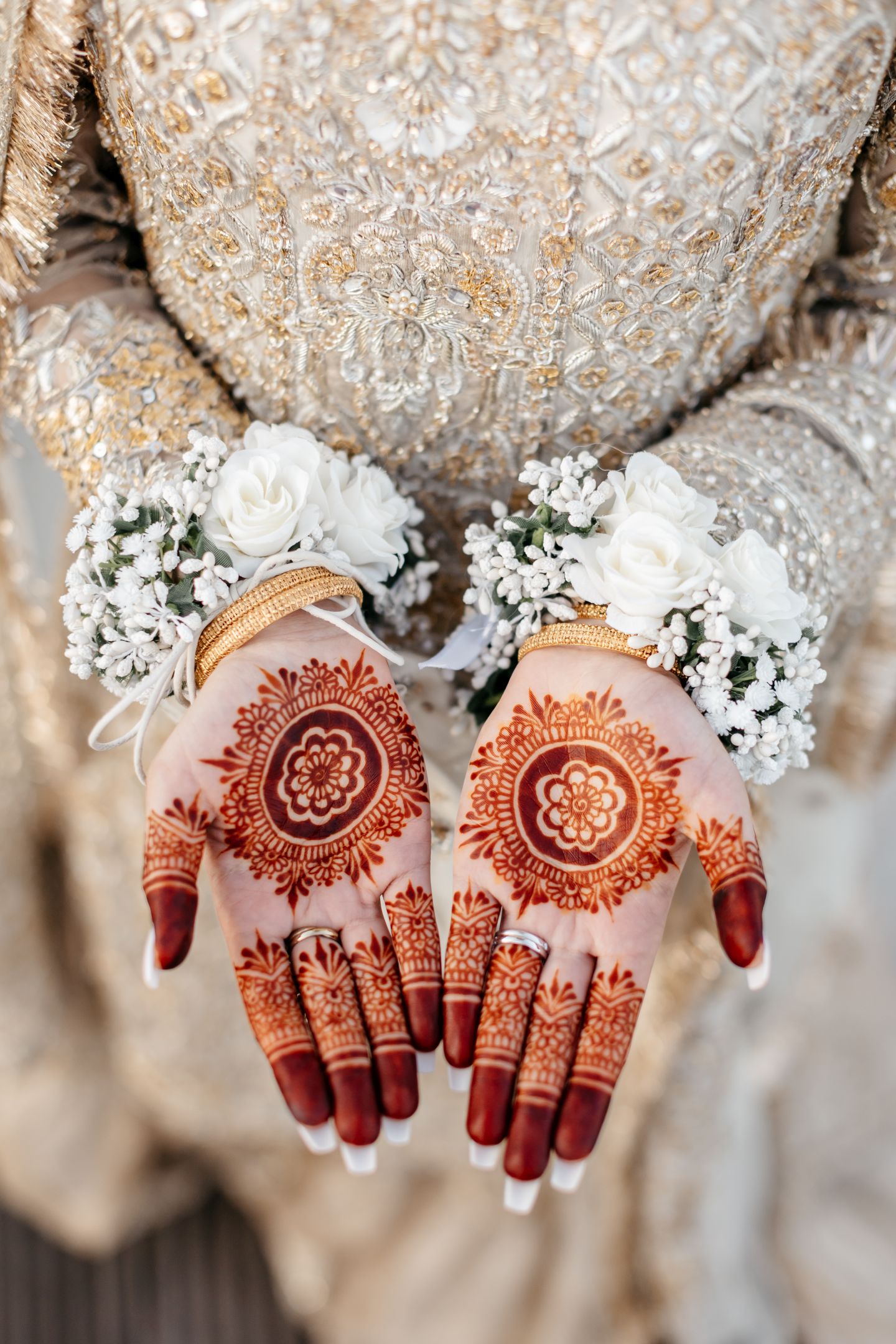 Close-up of bride's hands adorned with intricate mehndi henna and white floral wrist corsages