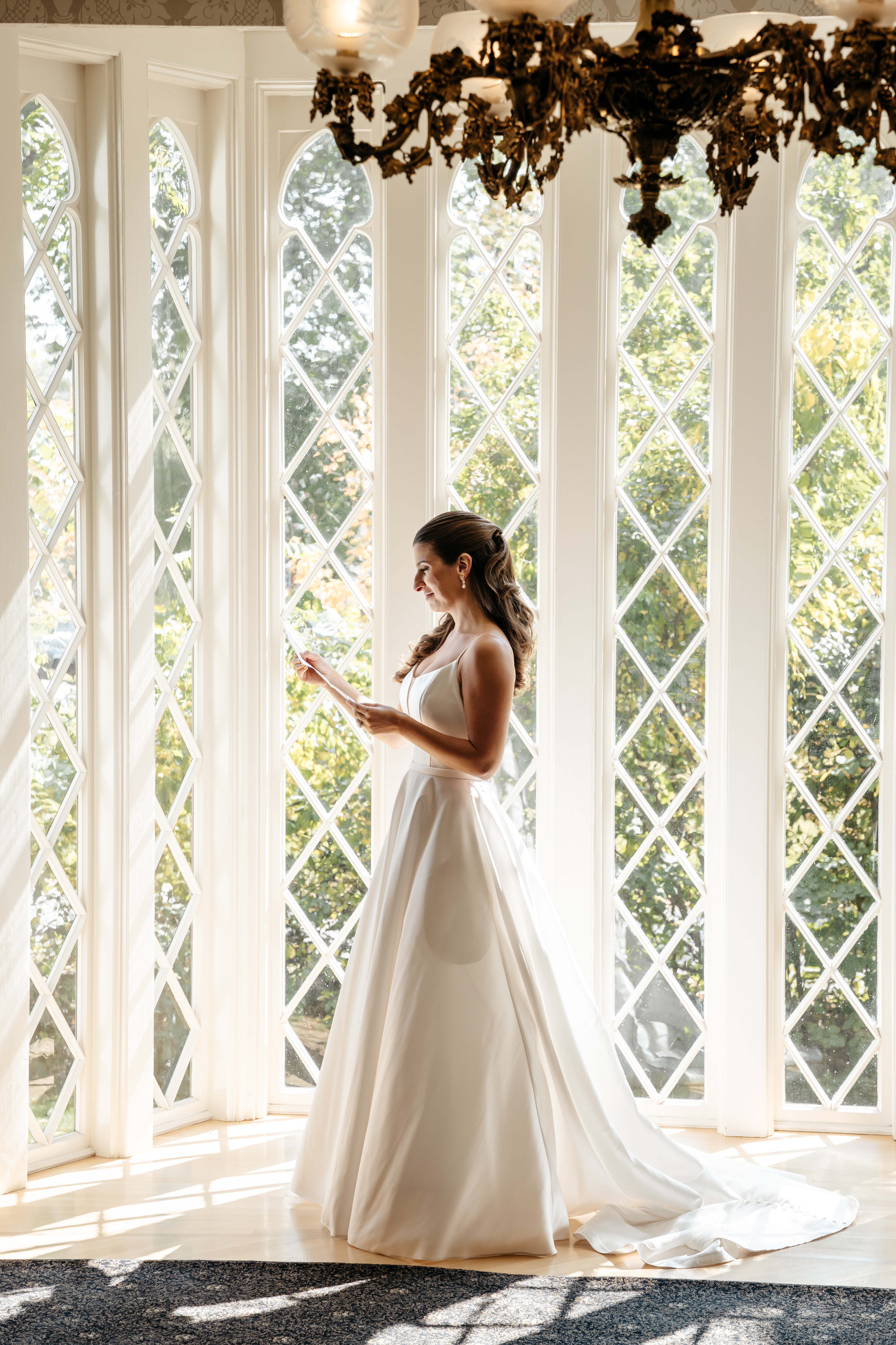 Bride in satin gown reading vows by cathedral windows