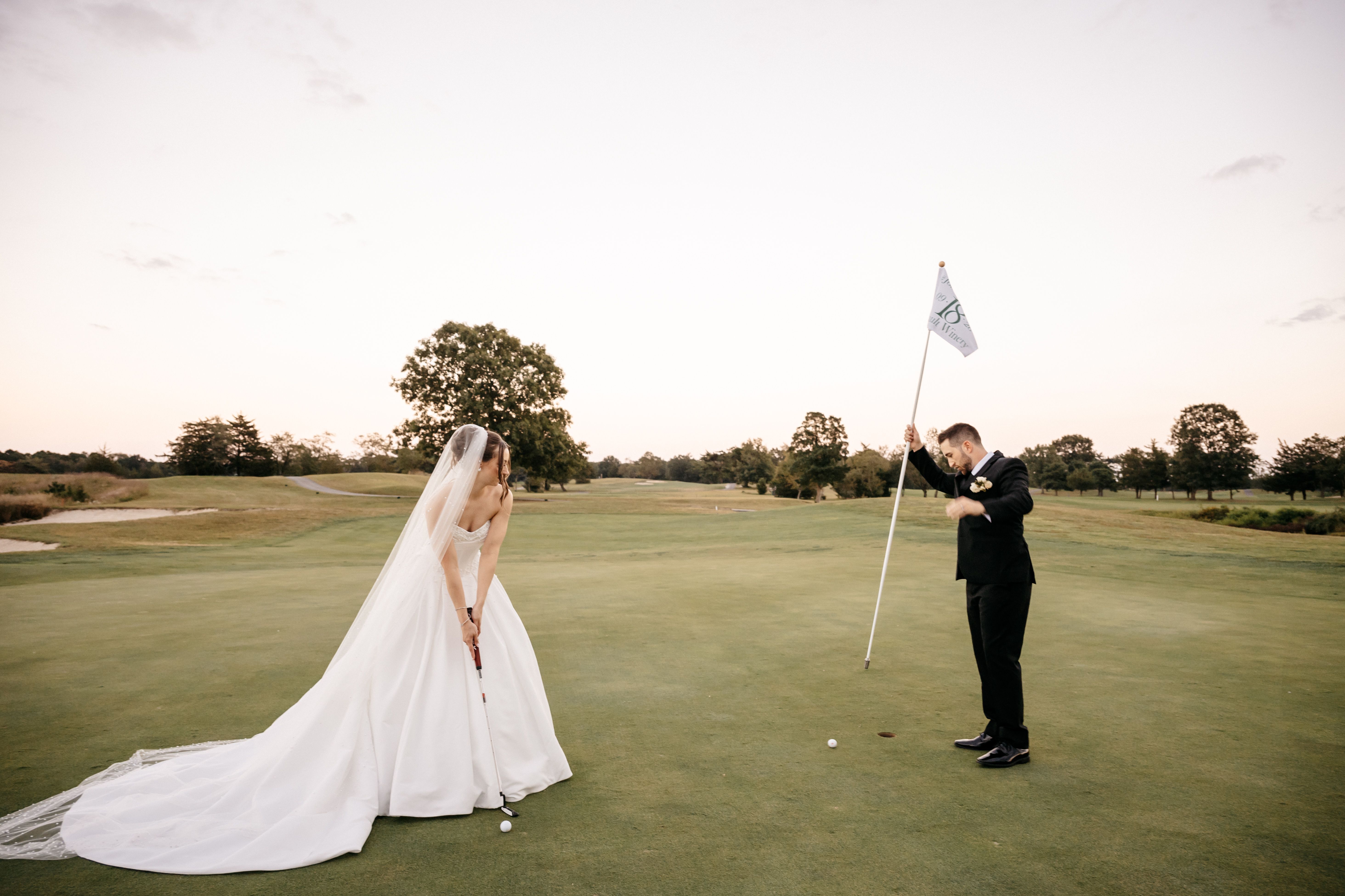 Bride putting on the golf green with groom tending the pin flag
