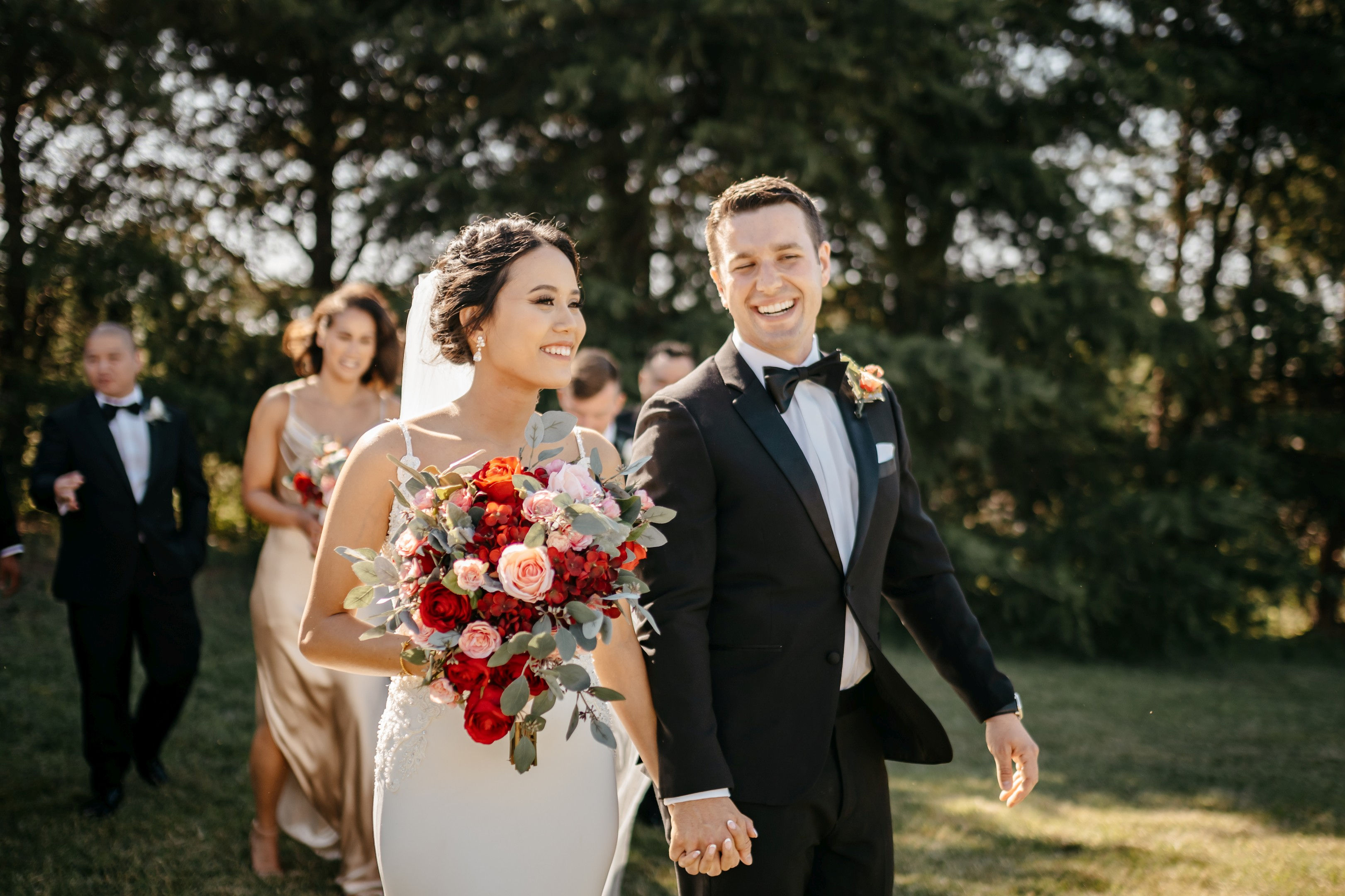 Joyful bride and groom holding hands with wedding party and floral bouquet