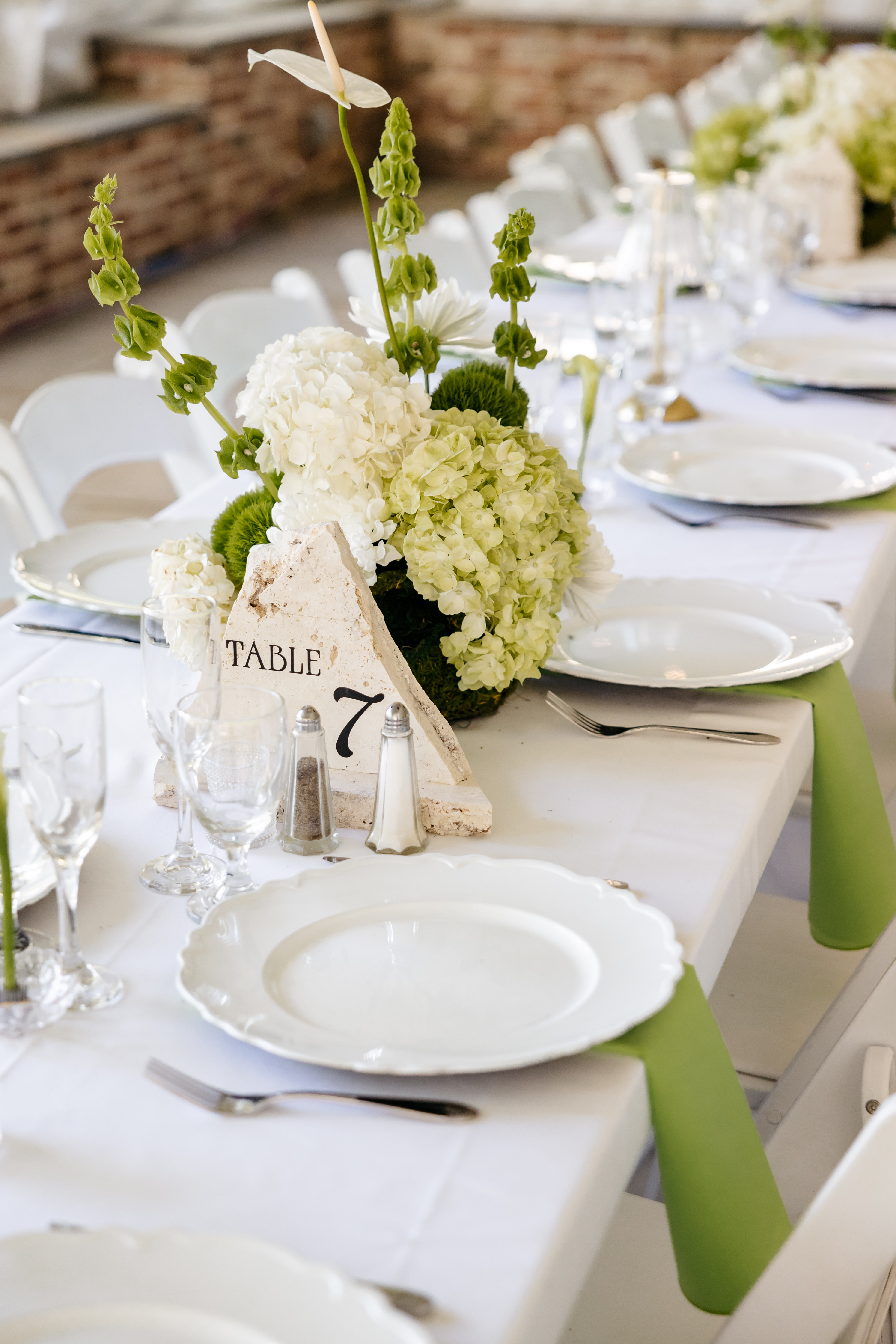 Reception table setting with fresh green hydrangeas and custom stone table number