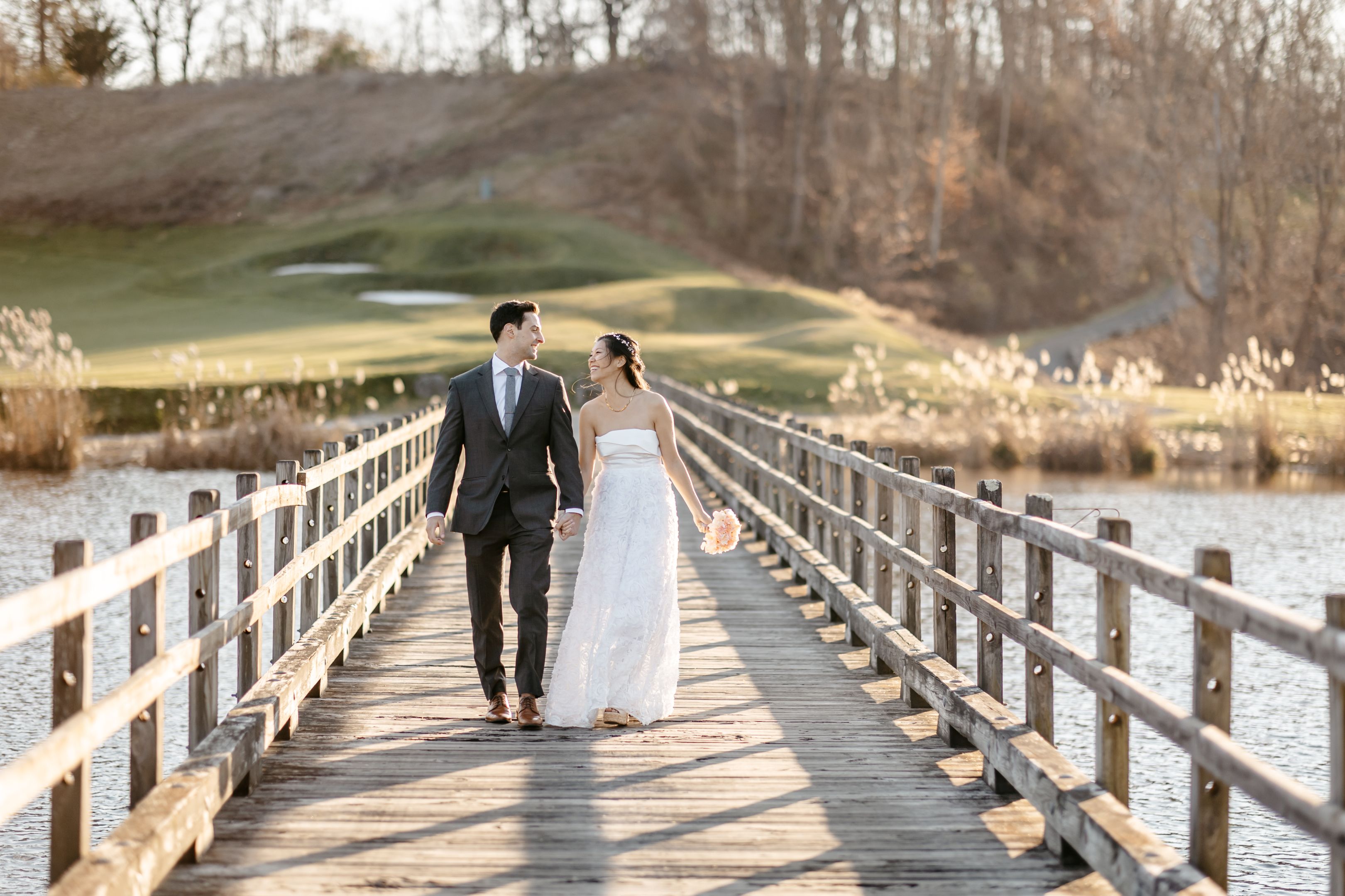 Bride and groom walking hand in hand across wooden dock bridge in Connecticut