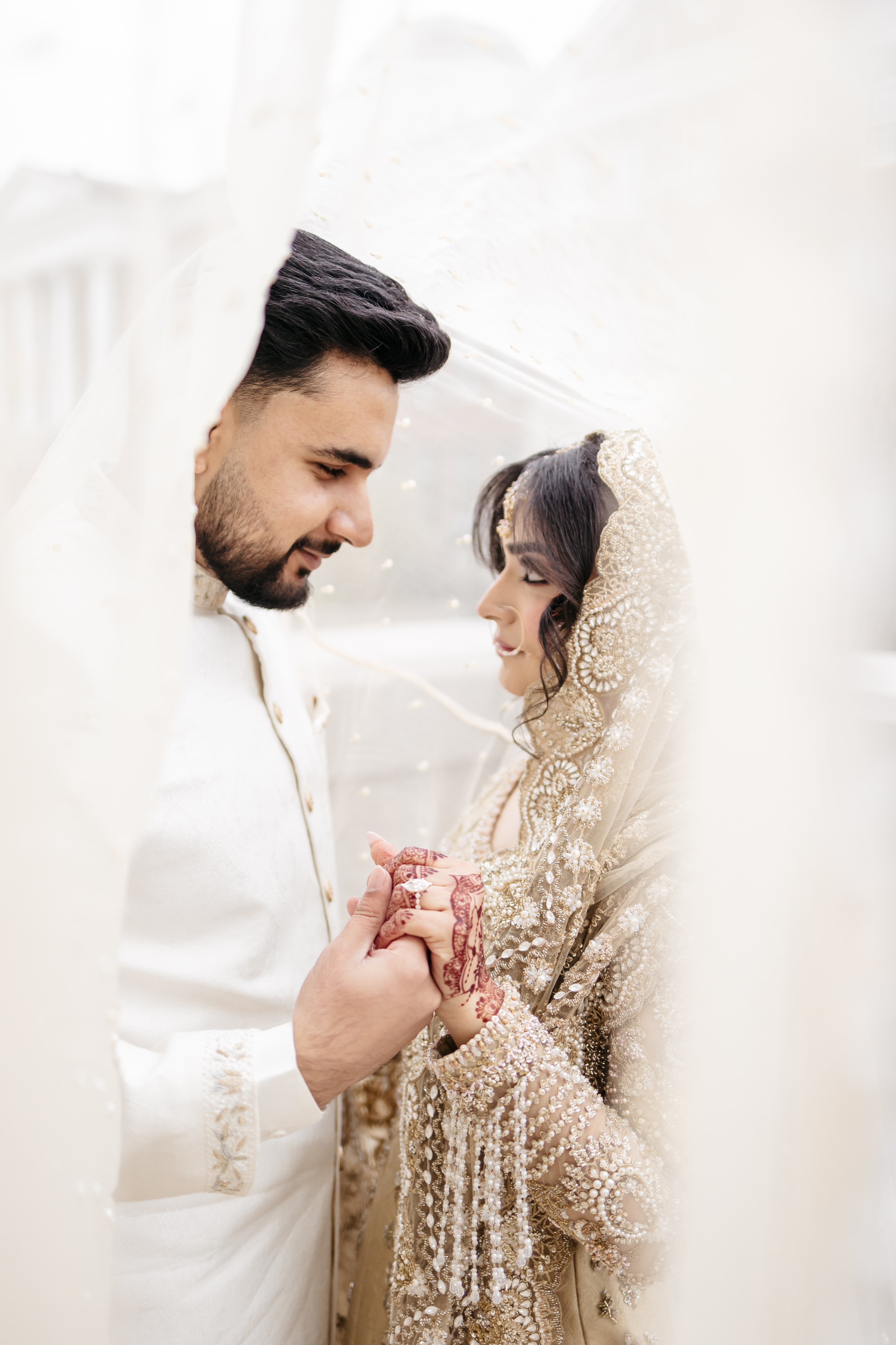 Romantic couple portrait under intricate bridal veil holding hands