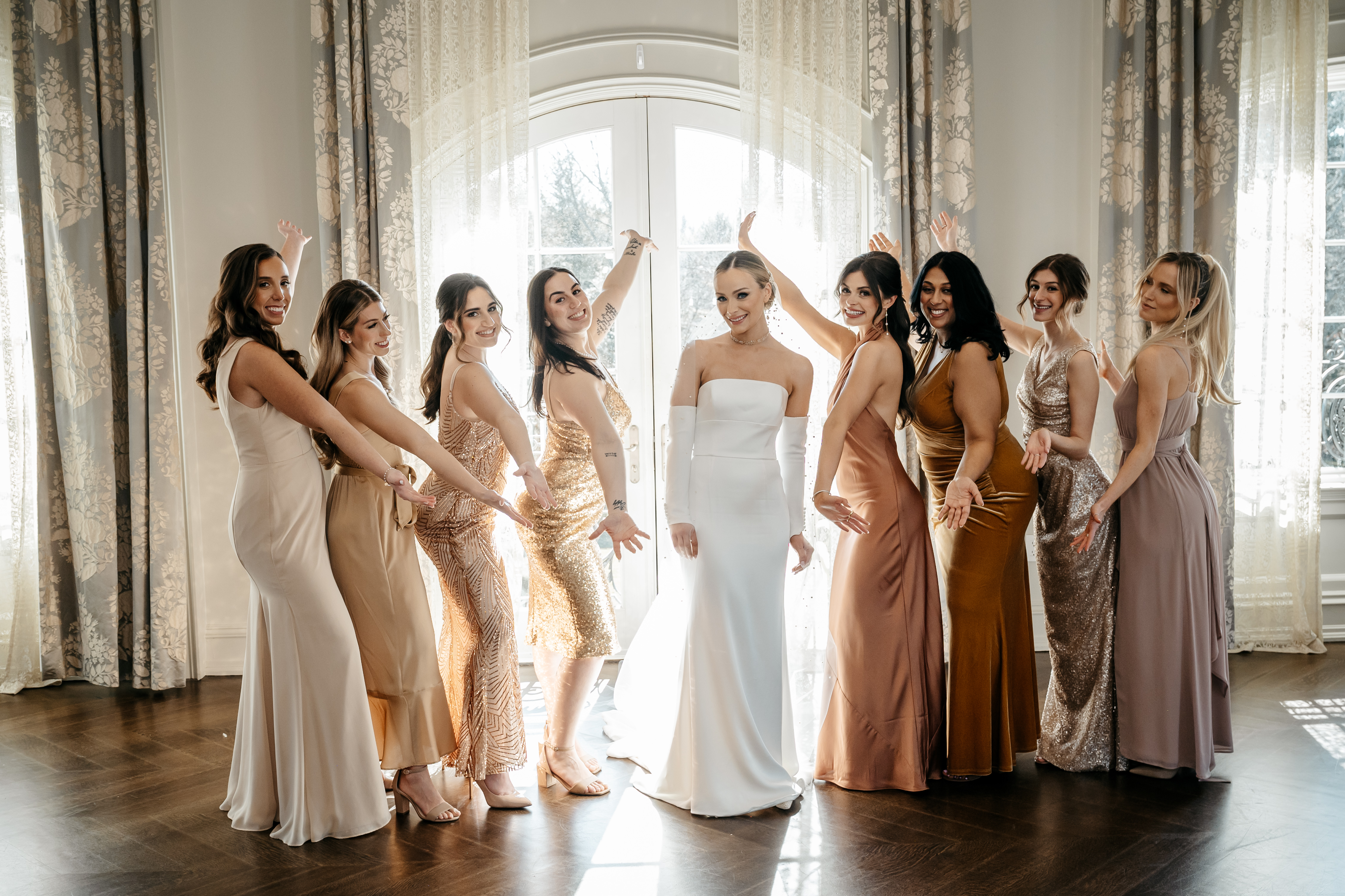 Joyful bride in white gown celebrated by bridesmaids in champagne and gold dresses