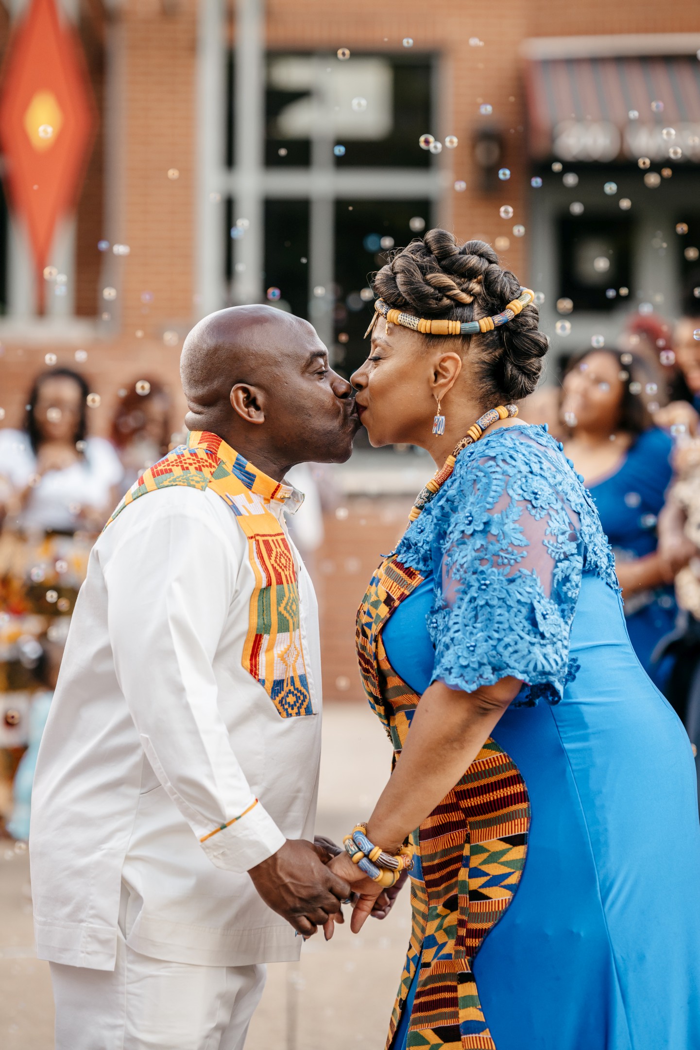 Bride and groom kissing outdoors in vibrant traditional attire surrounded by floating celebration bubbles
