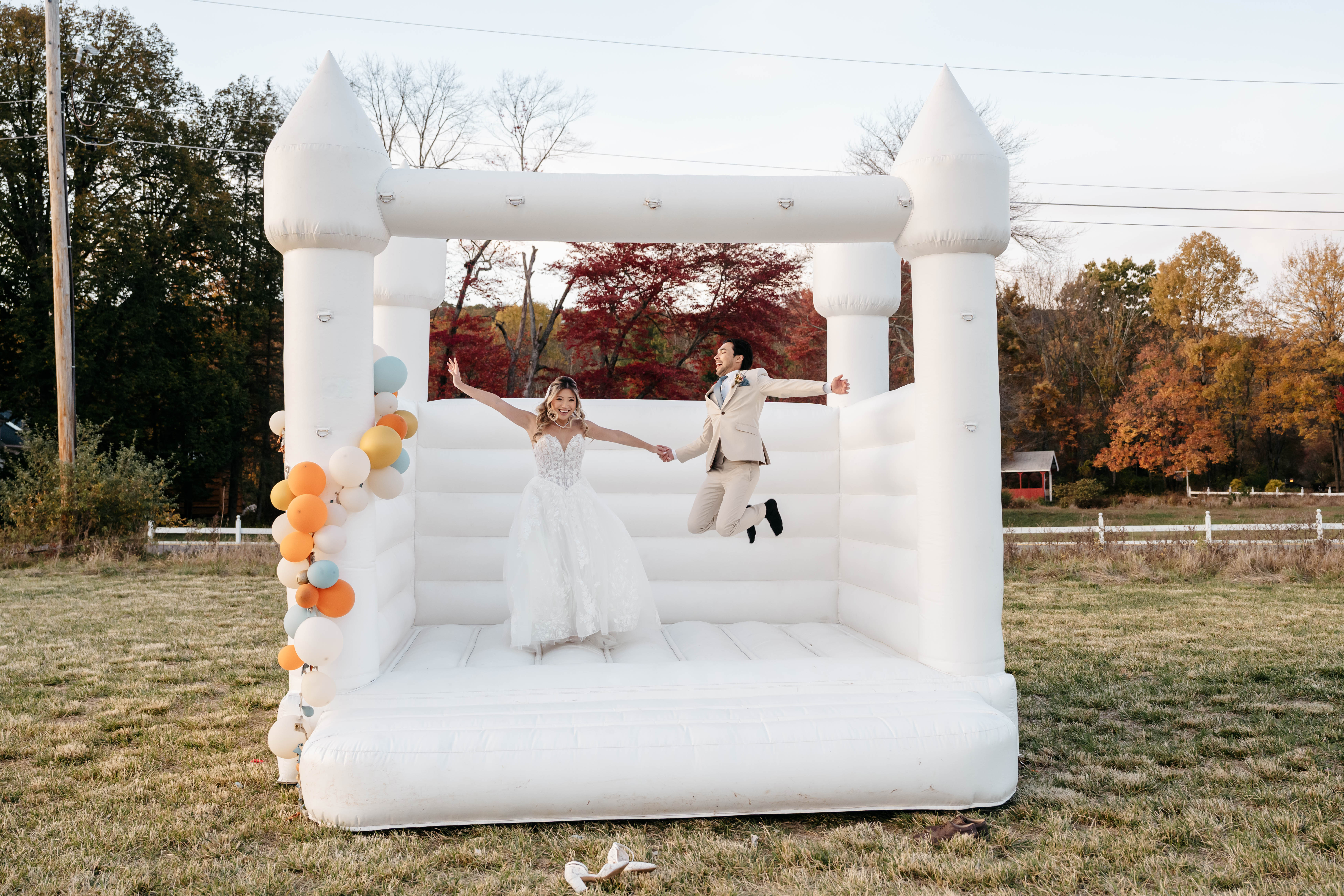 Joyful bride and groom jumping playfully in an all-white bouncy castle outdoors