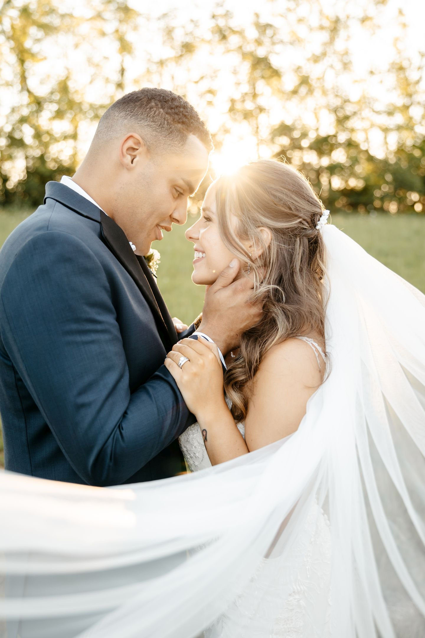 Golden hour sunset portrait of bride and groom embracing with veil