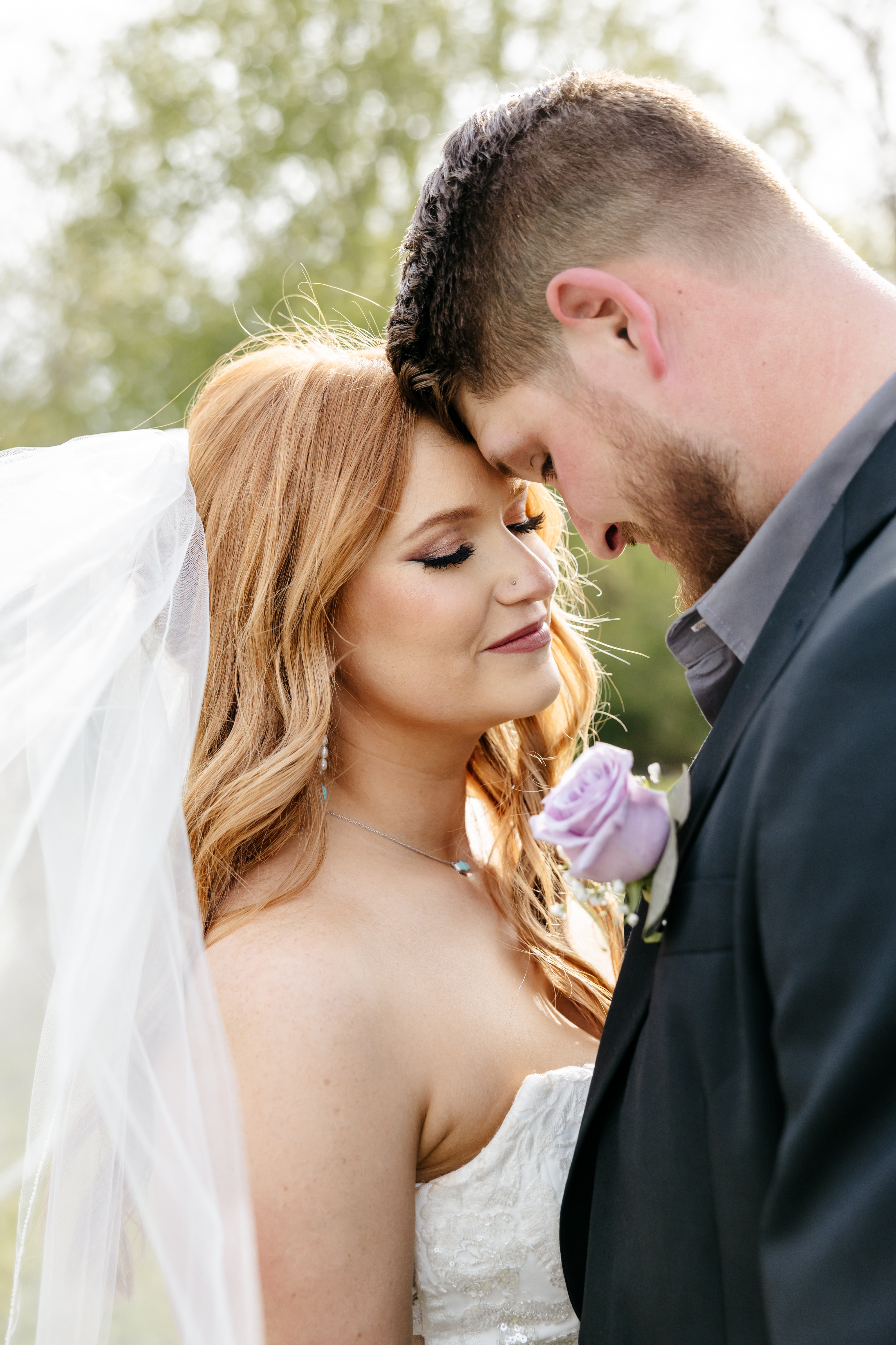 Beautiful portrait of bride in lace long-sleeve gown with hijab and groom in black tuxedo with white rose