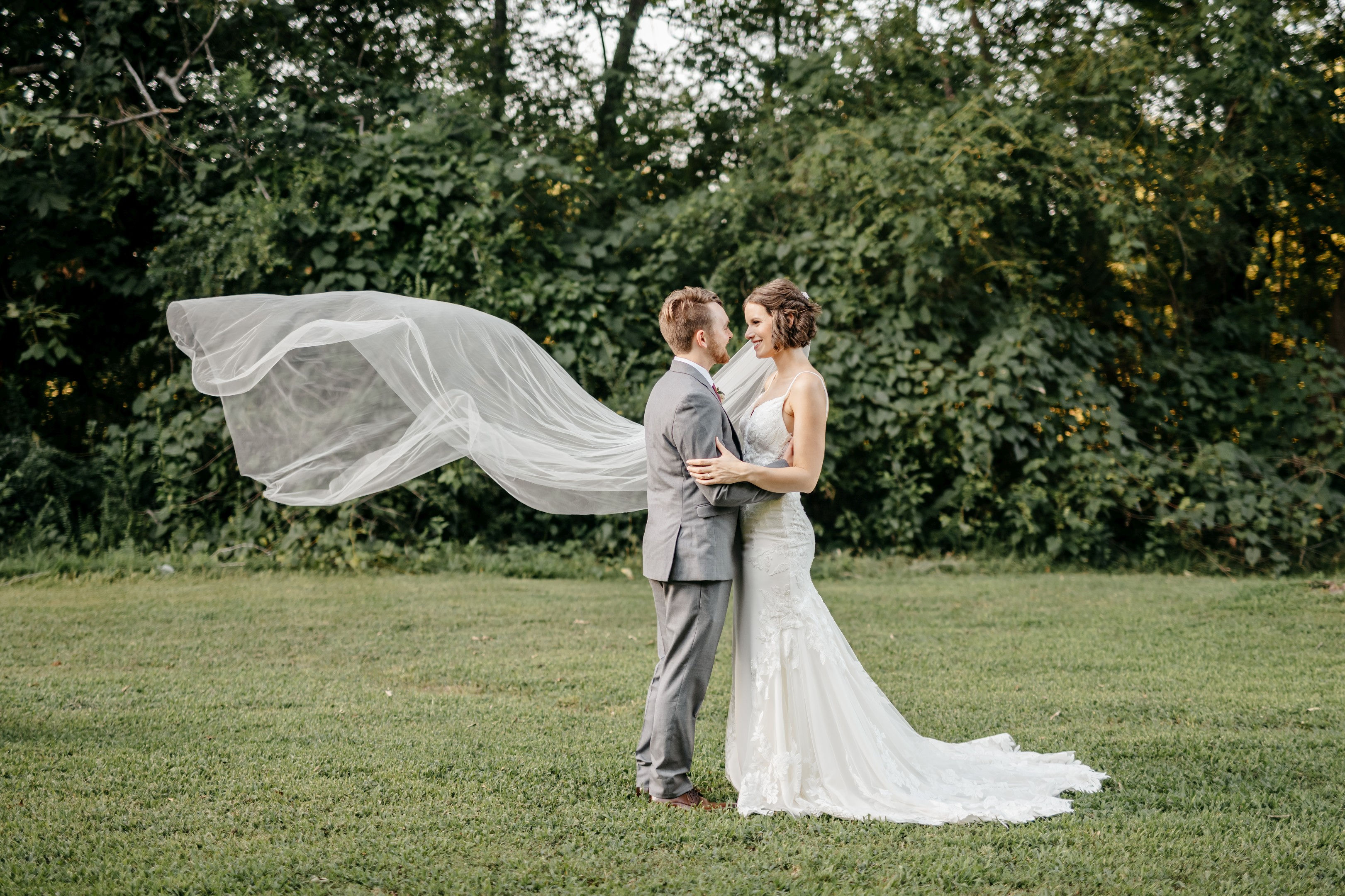Bride and groom standing together outdoors with flowing veil