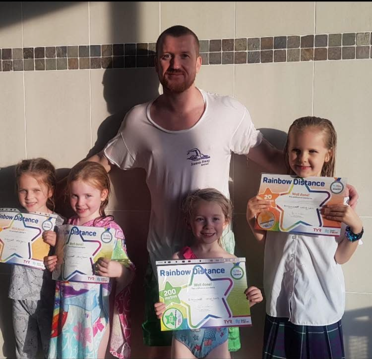 Benjamin Hamlett with young swimmers holding their distance certificates after a swimming lesson