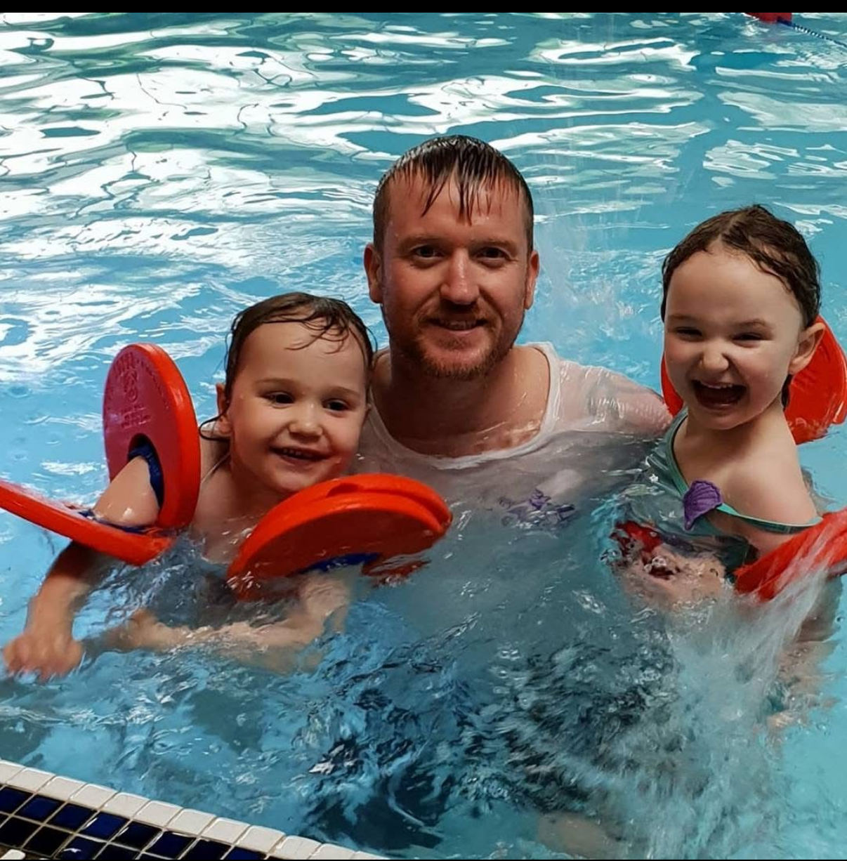 Benjamin Hamlett in the water supporting two young learners during a swimming lesson
