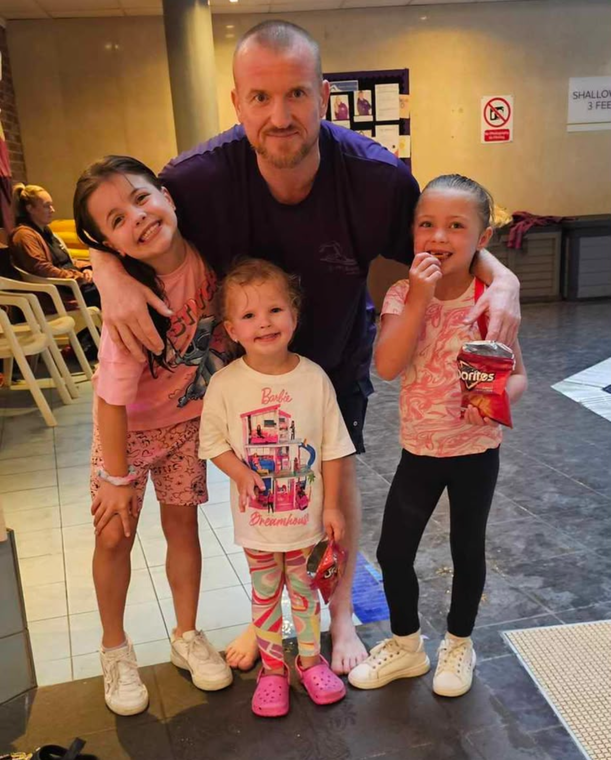 Benjamin Hamlett smiling poolside with three young swimming students