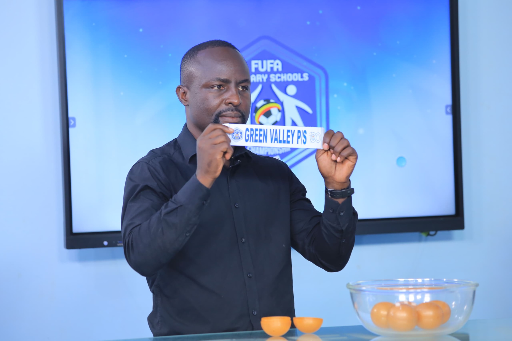Tonny Mawejje standing at a table during the FUFA 2024 Odilo Primary Schools Championship draw event, November 2024.
