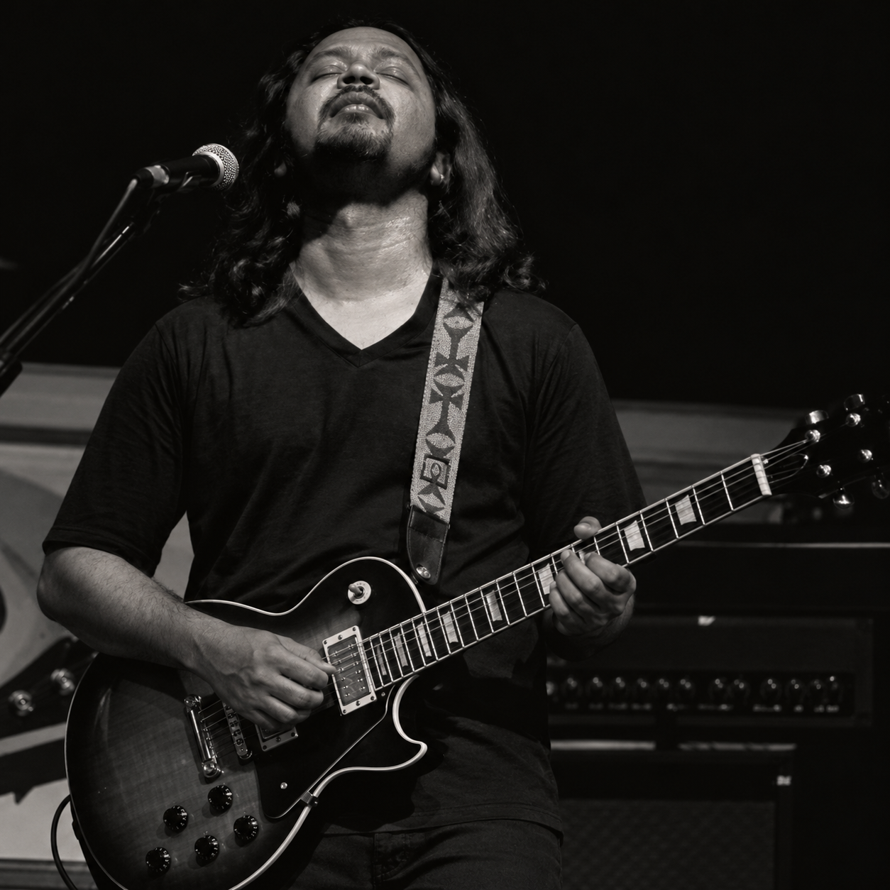 Black and white portrait of The Blue Mister playing guitar with eyes closed at the mic