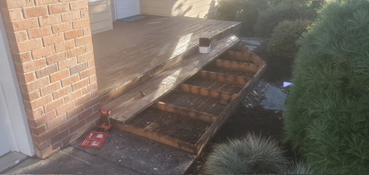 Front porch deck renovation showing exposed wooden framing and angled step joists along brick foundation