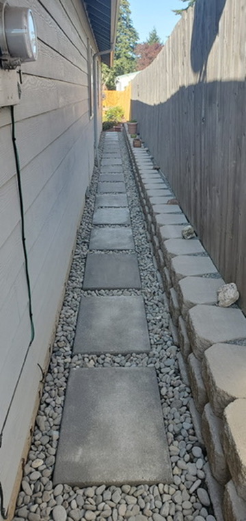 Finished side yard modern concrete stepping stones embedded in smooth river rock alongside retaining wall