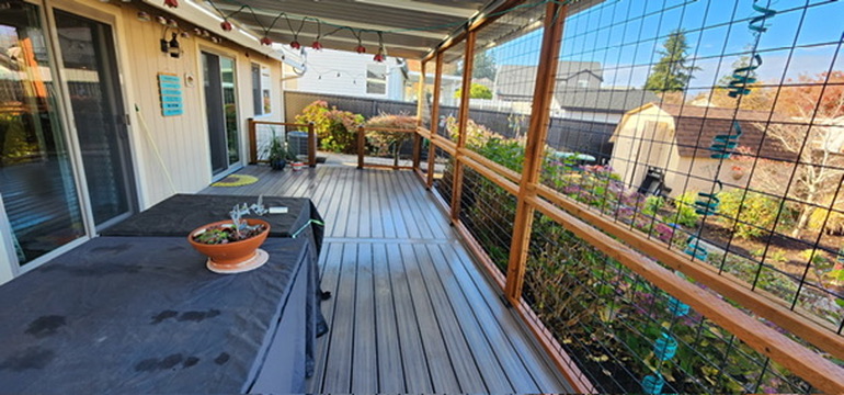 Wide panorama of completed covered composite deck with hog-wire railing and patio furniture