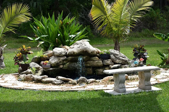 Hero's Mile peaceful outdoor stone fountain with gentle waterfall and reflection bench amidst tropical greenery