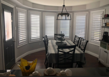 Multi-panel white custom shutters installed in curved bay dining room